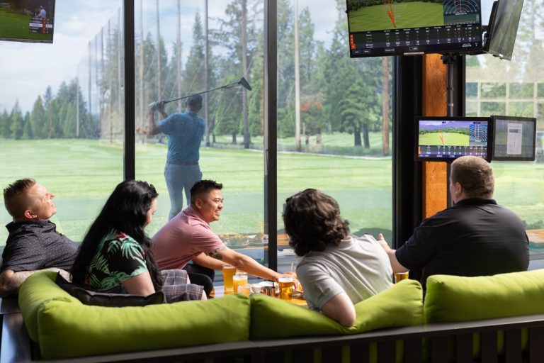5 people sitting on sofas in a lounge watching a golfer play outside